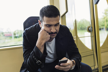 Junger Mann, der in der Straßenbahn eine Textnachricht über sein Mobiltelefon sendet - MASF03811