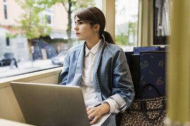 Junge Frau schaut durch ein Straßenbahnfenster und benutzt einen Laptop - MASF03812