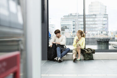 Frau schaut nach draußen, während sie mit ihrem Freund auf der Fensterbank des Bahnhofs sitzt - MASF03816