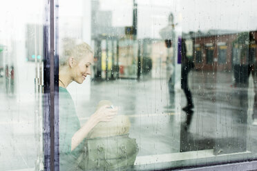 Junge Frau auf der Fensterbank sitzend, gesehen durch Glas am Bahnhof - MASF03818