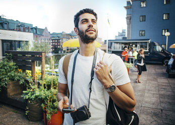 Tourist looking away while holding smart phone during vacation - MASF03825