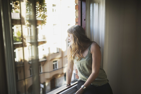 Young woman looking through window at home stock photo