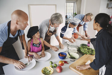 Woman guiding multi-generational family in preparing Asian food at kitchen - MASF03831