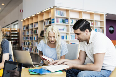 Junge Universitätsstudenten lesen ein Buch am Schreibtisch in der Bibliothek - MASF03843