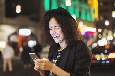 Junge Frau lacht bei der Benutzung eines Smartphones in einer nächtlichen Stadt - MASF03850