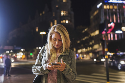 Frau benutzt Smartphone auf einer nächtlichen Straße in der Stadt, lizenzfreies Stockfoto