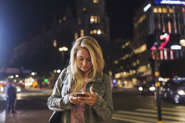 Woman using smart phone on city street at night - MASF03852