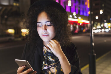 Woman using smart phone sidewalk in city at night - MASF03854