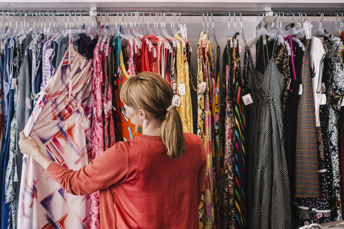 Frau betrachtet ein Kleid, das auf einem Ständer hängt, während sie in einem Geschäft steht - MASF03855