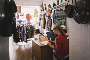 Frau arbeitet am Schreibtisch und sitzt in einem Secondhand-Laden - MASF03857