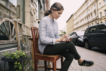 Frau liest Zeitung und sitzt auf einem Stuhl vor einem Geschäft in der Stadt - MASF03860