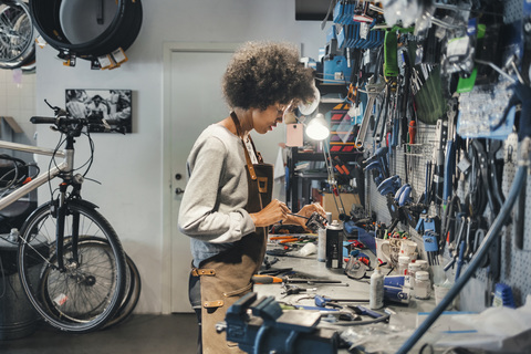 Seitenansicht einer Mechanikerin bei der Arbeit in einer Fahrradwerkstatt, lizenzfreies Stockfoto