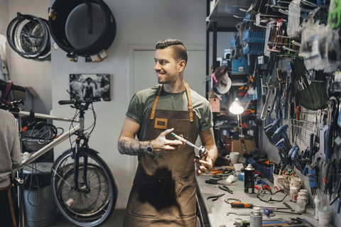 Lächelnder männlicher Mechaniker, der seinen Kollegen bei der Reparatur eines Pedals in der Werkstatt ansieht, lizenzfreies Stockfoto