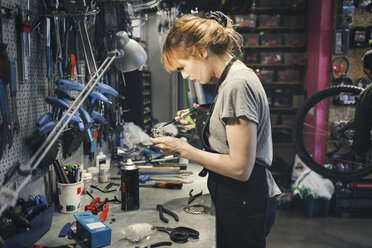 Seitenansicht einer Mechanikerin beim Ölen des Pedals in der Werkstatt - MASF03868