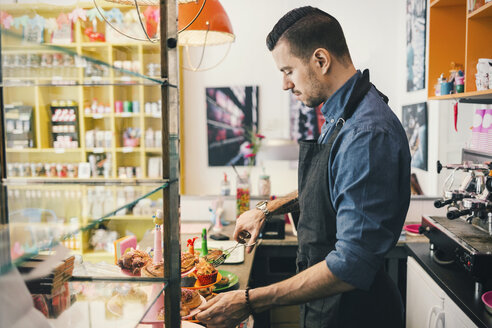 Side view of male barista using tongs to remove cupcake at cafe counter - MASF03869