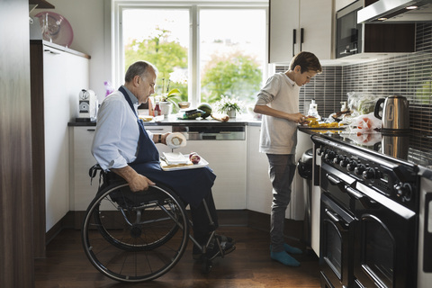 Sohn mit behindertem Vater beim Gemüseschneiden in der Küche, lizenzfreies Stockfoto