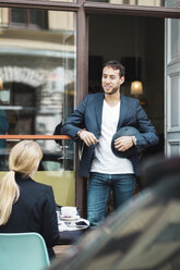 Lächelnder Geschäftsmann mit Helm im Gespräch mit einem Kollegen in einem Straßencafé - MASF03878