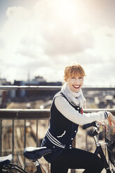 Seitenansicht Porträt der glücklichen Geschäftsfrau stehend mit Fahrrad auf Brücke gegen Himmel - MASF03879