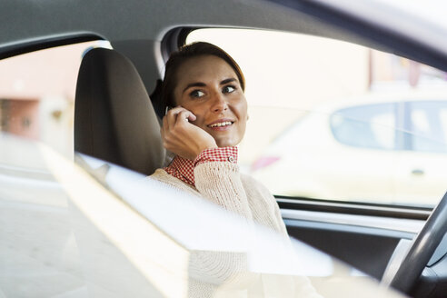 Lächelnde Geschäftsfrau schaut weg, während sie ihr Smartphone im Auto benutzt - MASF03896