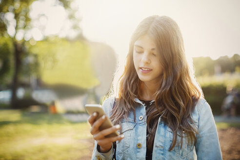 Teenager, der im Park steht und sein Smartphone benutzt - MASF03898