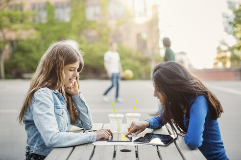 Seitenansicht von weiblichen Teenagern, die ein digitales Tablet an einem Tisch im Freien benutzen - MASF03900
