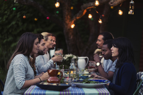 Seitenansicht von glücklichen multiethnischen Freunden beim Abendessen am Tisch im Hof, lizenzfreies Stockfoto