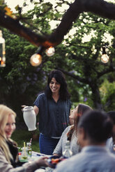 Lächelnde Frau, die einen Krug hält, während Freunde während einer Party am Esstisch sitzen - MASF03916