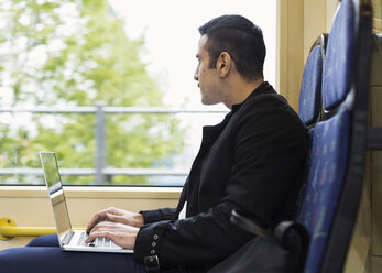 Side view of young man using laptop while looking through tram window - MASF03920
