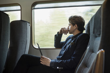 Side view of thoughtful businessman holding digital tablet in train - MASF03939