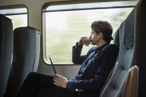 Seitenansicht eines nachdenklichen Geschäftsmannes, der ein digitales Tablet im Zug hält - MASF03939
