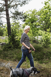 Seitenansicht einer glücklichen älteren Frau, die mit ihrem Hund auf einem Feld spazieren geht - MASF03945