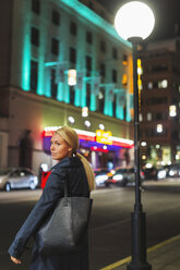 Side view of woman standing on sidewalk in city during night - MASF03947