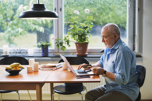 Side view of senior man using credit card for online shopping at home - MASF03956