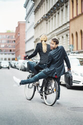 Rückansicht eines glücklichen Geschäftsmannes, der auf dem Rücksitz sitzt, während eine Kollegin Fahrrad fährt - MASF03962