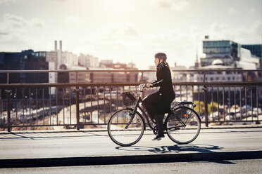 Seitenansicht einer Geschäftsfrau, die auf einer Brücke in der Stadt Fahrrad fährt - MASF03963