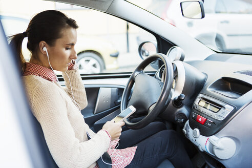 Seitenansicht einer Geschäftsfrau, die beim Autofahren Musik über ihr Smartphone hört - MASF03986