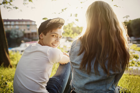 Rückansicht eines glücklichen Teenagers, der mit einer Freundin am Seeufer sitzt - MASF03990