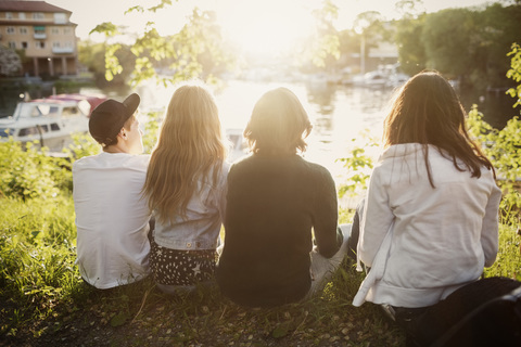 Rear view of teenagers sitting at lakeshore stock photo