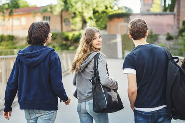 Rear view portrait of smiling female teenager walking with male friends on bridge - MASF03998
