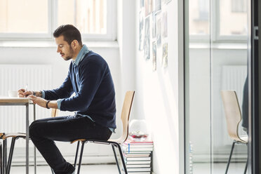 Side view of businessman writing in book at office desk - MASF03999