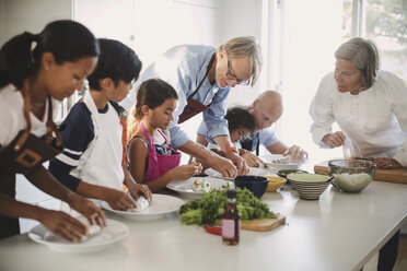 Senior woman guiding family in preparing Asian food in kitchen - MASF04012