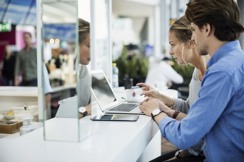 Seitenansicht von Geschäftsleuten mit Kreditkarte und Laptop in der Flughafenlobby, lizenzfreies Stockfoto