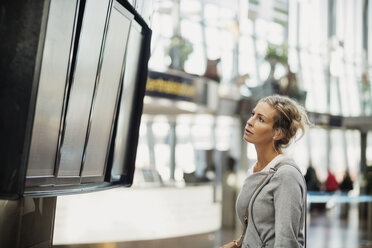 Seitenansicht einer Geschäftsfrau, die die Ankunfts- und Abflugtafel am Flughafen liest - MASF04016