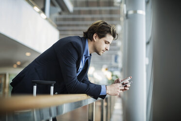 Side view of businessman using mobile phone while leaning on railing at airport - MASF04018