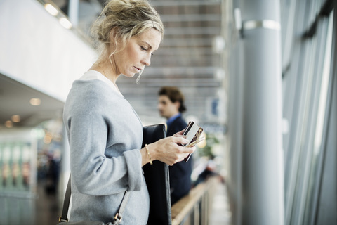 Seitenansicht einer Geschäftsfrau, die ein Smartphone am Flughafen benutzt, lizenzfreies Stockfoto