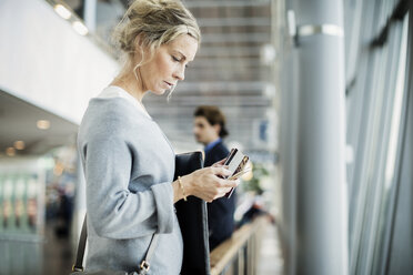 Seitenansicht einer Geschäftsfrau, die ein Smartphone am Flughafen benutzt - MASF04019