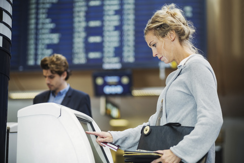 Seitenansicht einer Geschäftsfrau, die einen Check-in-Automaten am Flughafen benutzt, lizenzfreies Stockfoto