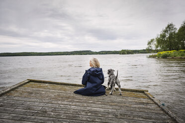 Rückansicht einer älteren Frau und eines Hundes auf einem Steg am See gegen einen bewölkten Himmel - MASF04027