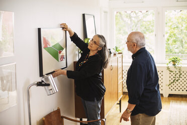 Älterer Mann betrachtet Frau, die zu Hause einen Bilderrahmen aufhängt - MASF04032