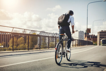 Rear view of businessman riding bicycle on bridge in city - MASF04048